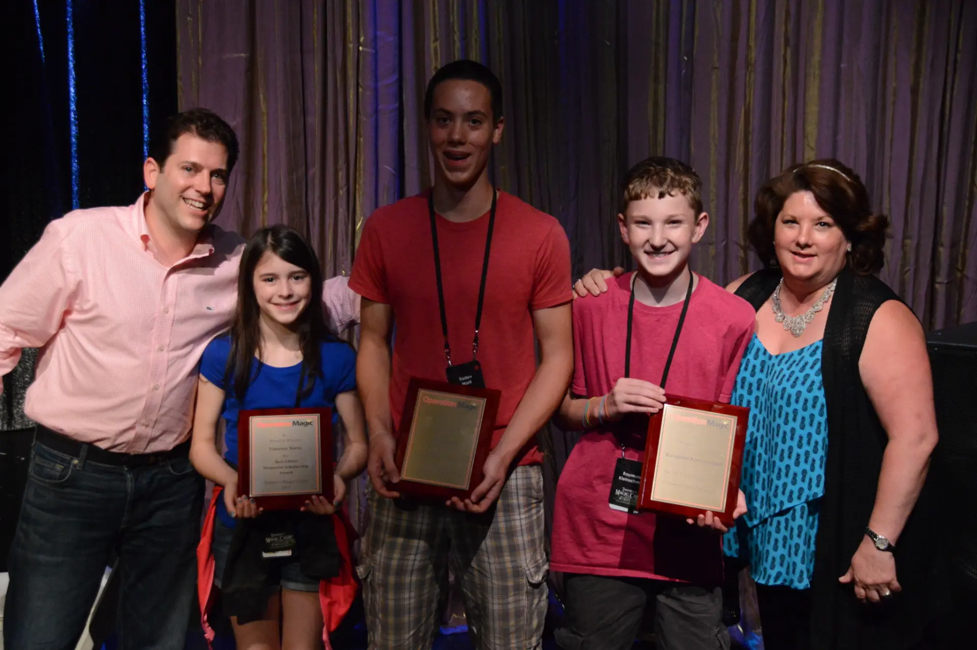 Operation Magic scholarship winners on stage holding their engraved plaques alongside two presenters
