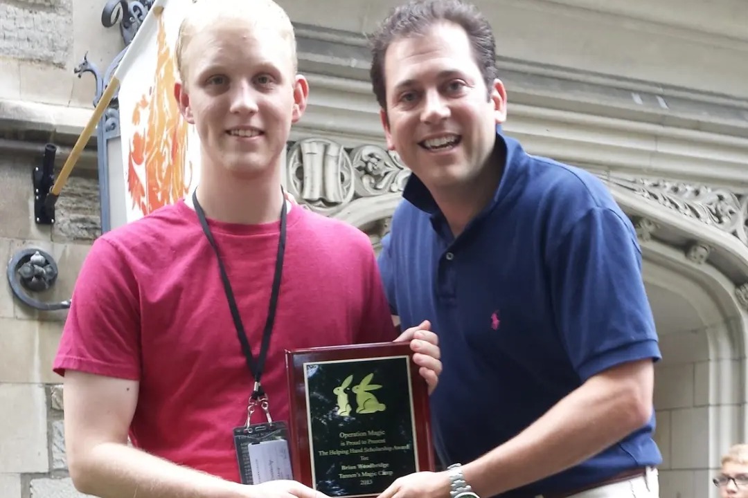 A scholarship recipient holding his Operation Magic plaque beside a presenter
