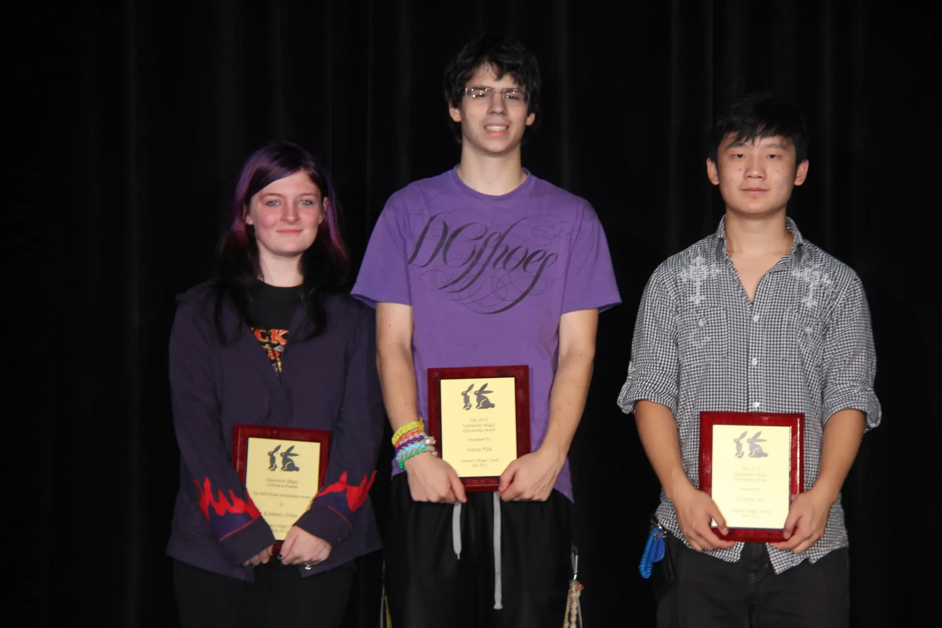 Three magic camp scholarship recipients on stage, each holding an Operation Magic award plaque